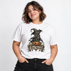 Model wearing a white T-shirt with a witch cat sitting on a pumpkin, skulls, autumn leaves, and a Stay Spooky banner.
