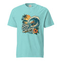 Front of a Lagoon Blue T-shirt with a surfer riding a curling wave, palm trees, sunset, tropical flowers, and “Stay Surfing” text.