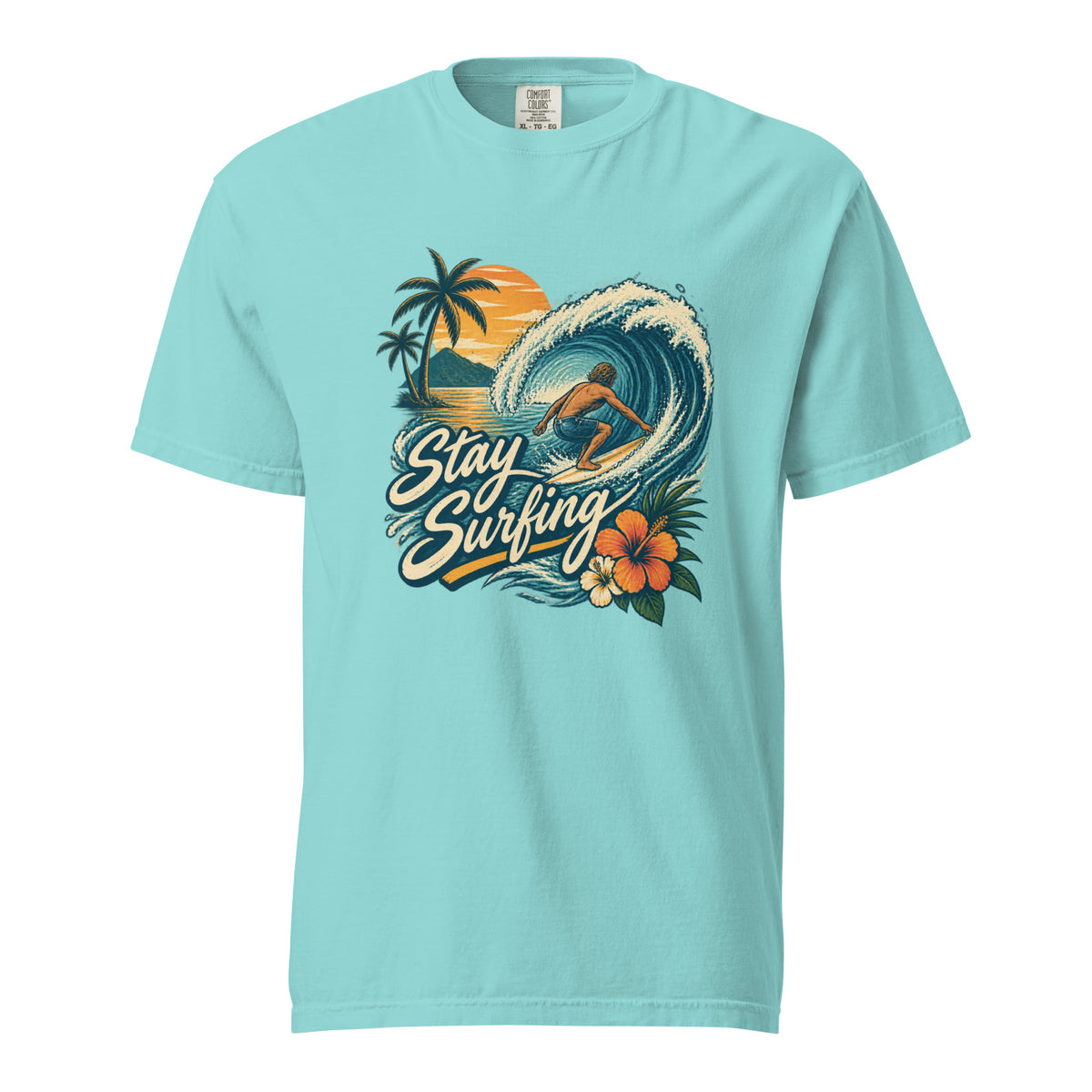 Front of a Lagoon Blue T-shirt with a surfer riding a curling wave, palm trees, sunset, tropical flowers, and “Stay Surfing” text.