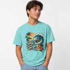 Surfer Riding Wave t shirt in Lagoon Blue worn by a studio model in an upper-body hands in pockets pose on a clean white background