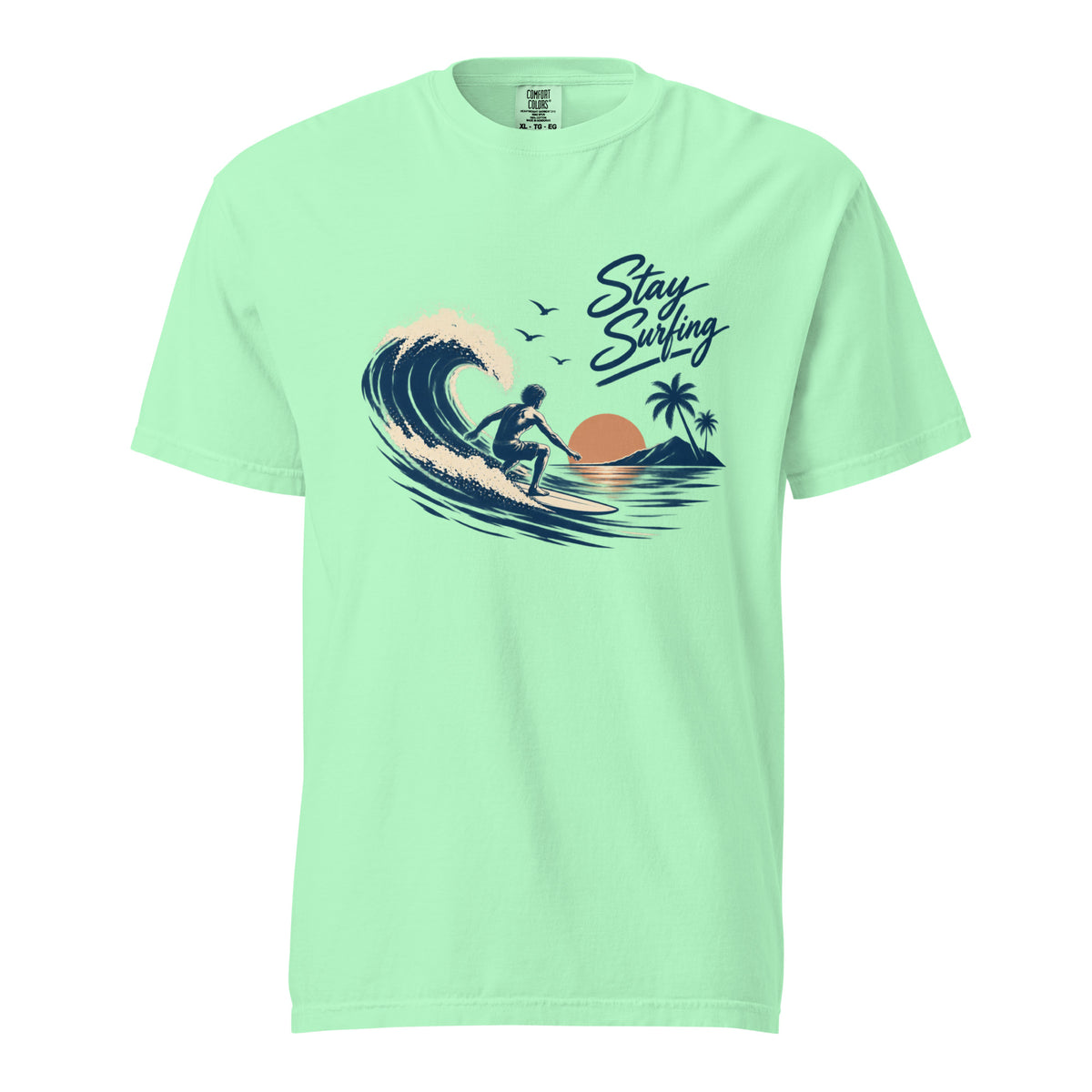 Front view of an Island Reef T-shirt featuring a surfer riding a wave, palm tree, setting sun, birds, and “Stay Surfing” lettering.