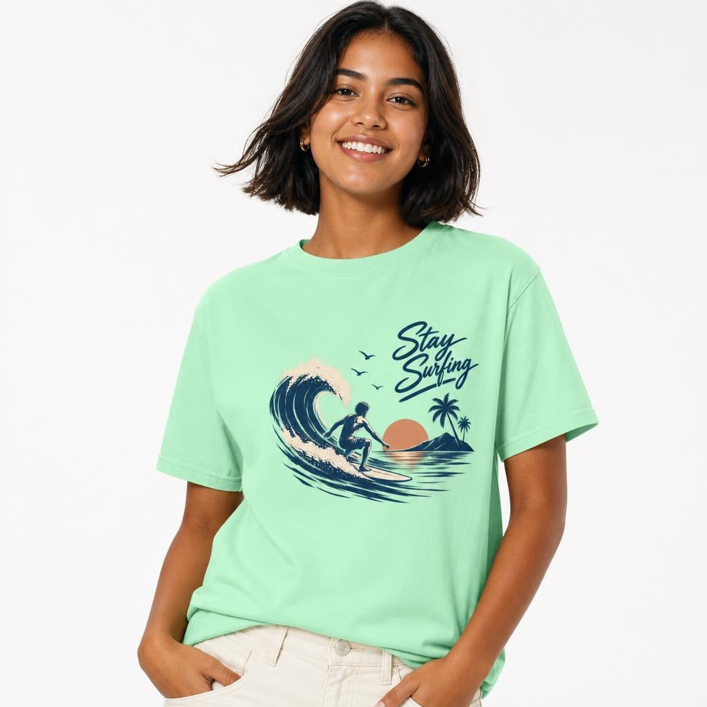 Model wearing an Island Reef T-shirt featuring a surfer riding a curling wave with palm trees and “Stay Surfing” script.