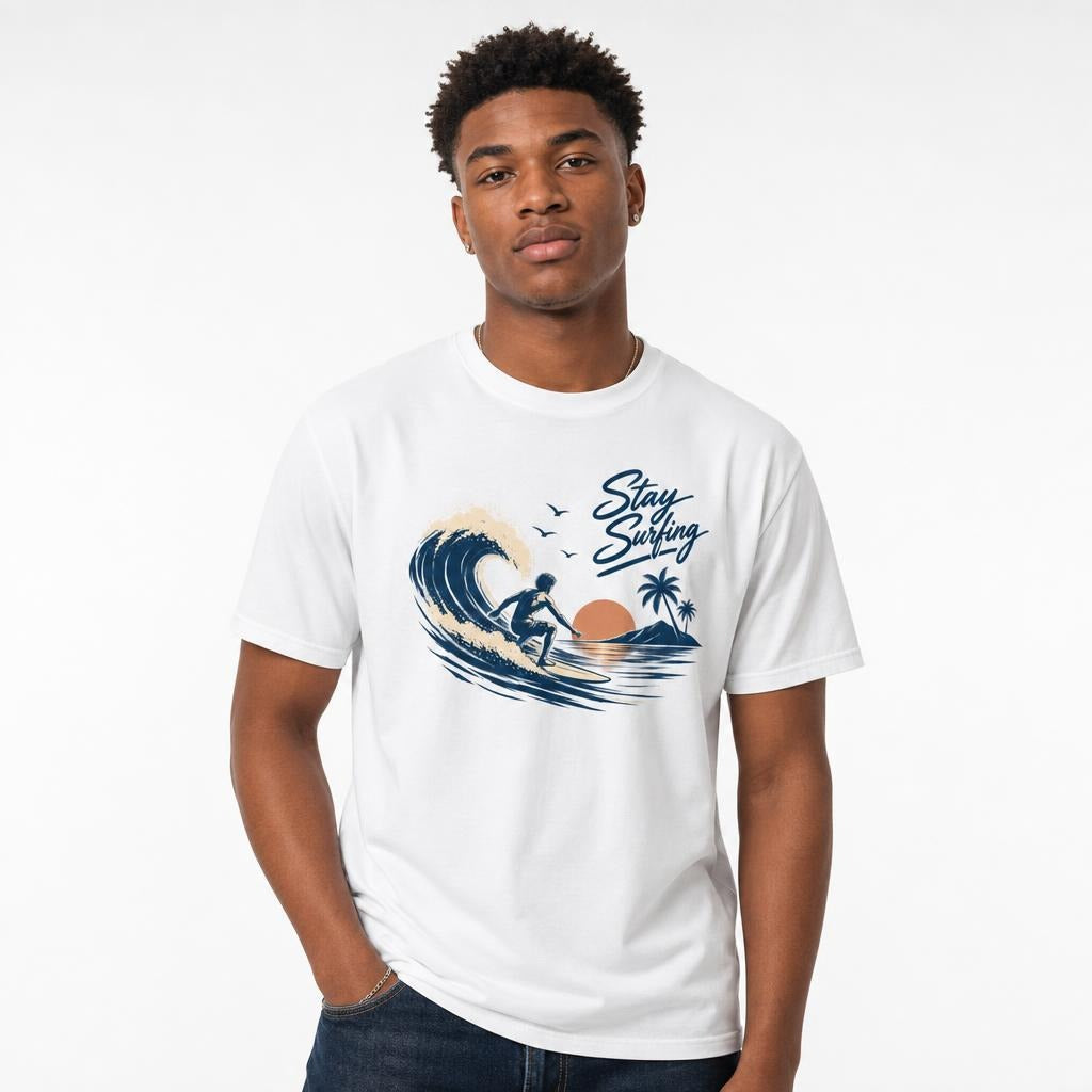 Model wearing a white T-shirt with a Stay Surfing graphic showing a surfer riding a wave beside palm trees and a sunset.