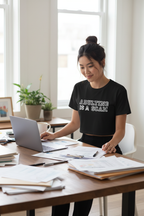Model wearing the Adulting Is A Scam black crop top beside a desk in a workspace scene