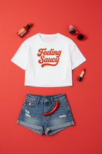 Feeling Saucy Retro Script Crop Top flat lay styled with denim shorts on an orange background
