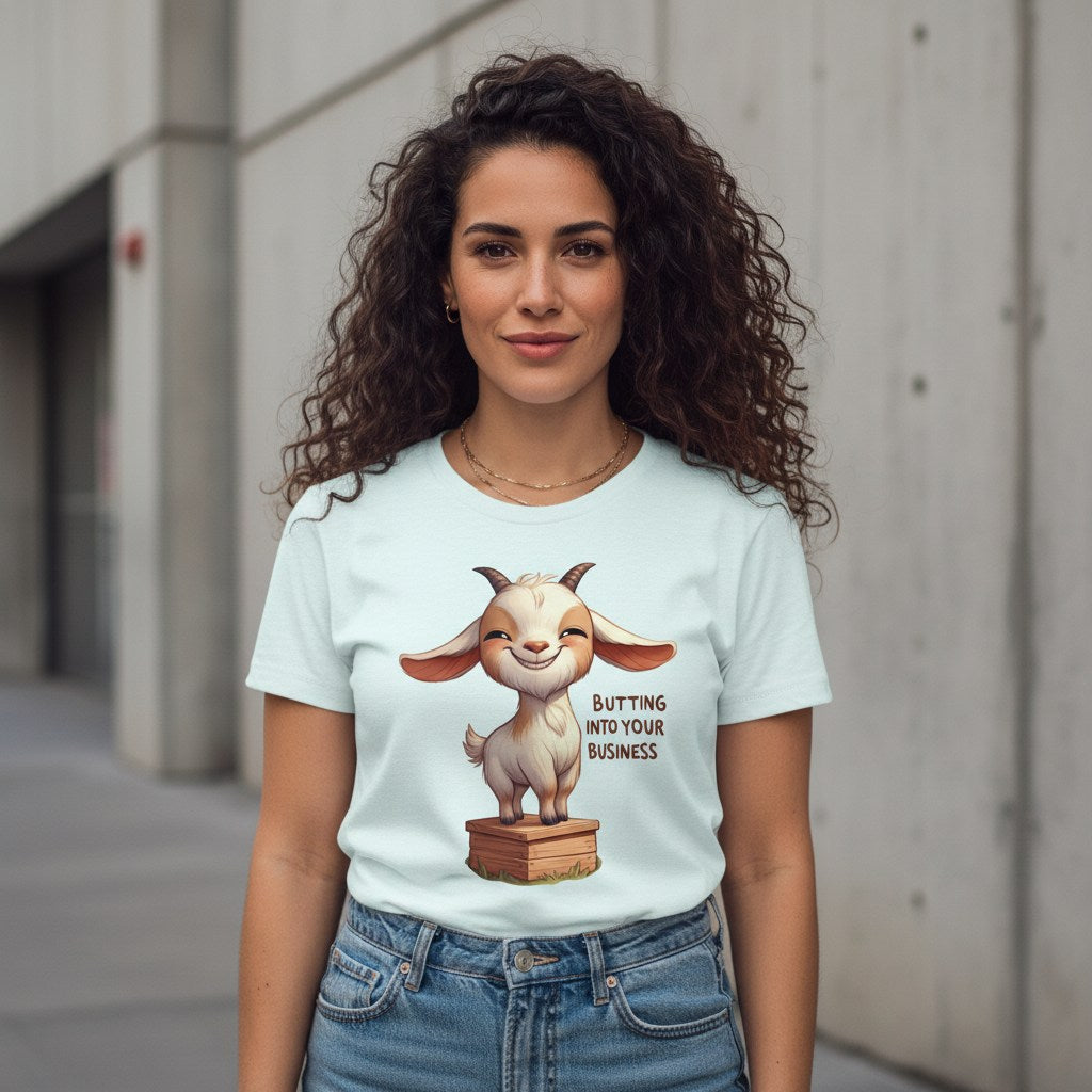 Woman wearing a light blue t-shirt with a cartoon goat graphic and text, standing against a concrete wall.