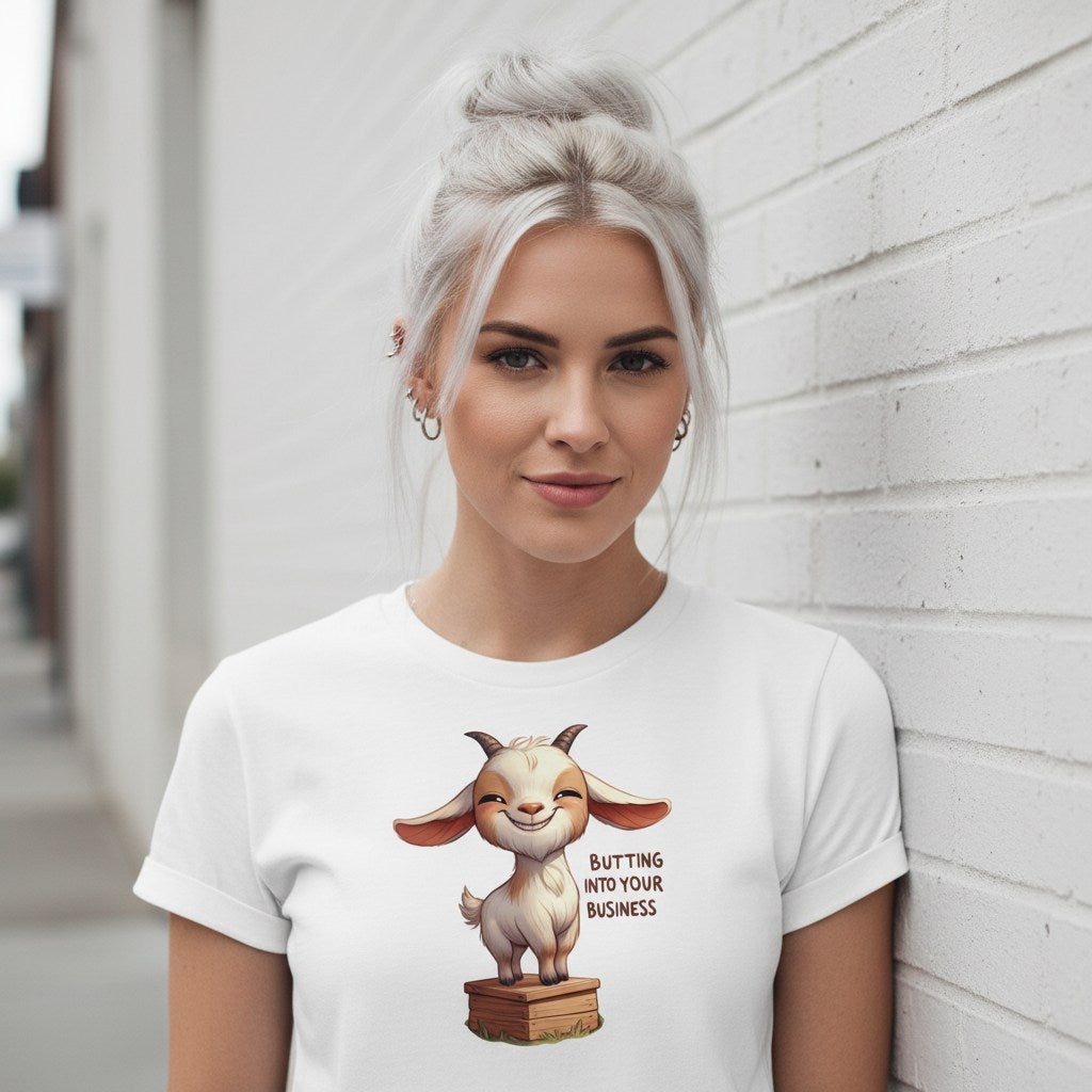 Woman wearing a white t-shirt with a cartoon goat graphic and text, standing against a light-colored wall.