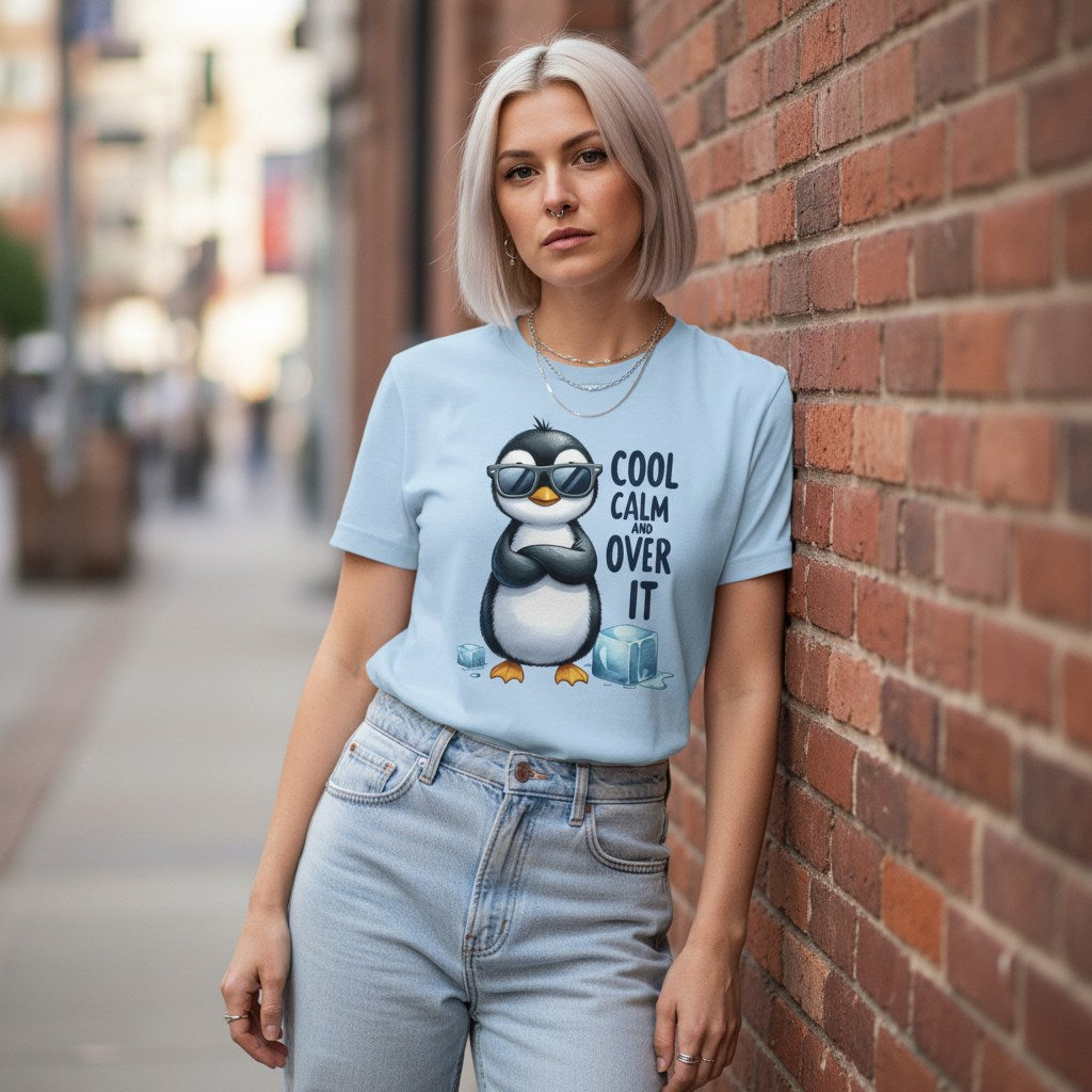 Woman wearing a light blue t-shirt with a penguin graphic and text, leaning against a brick wall.