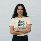 Woman wearing a yellow t-shirt with a penguin graphic and text against a white wall.