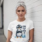 Woman wearing a white t-shirt with a penguin graphic and text, leaning against a light gray wall.