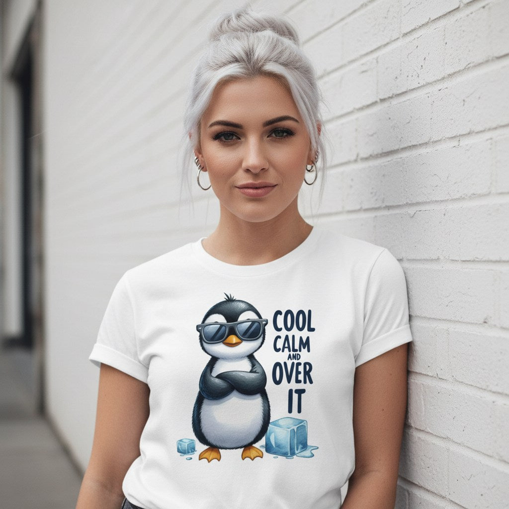 Woman wearing a white t-shirt with a penguin graphic and text, leaning against a light gray wall.