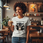 Woman in a coffee shop wearing a t-shirt with a cat graphic and text.