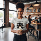 Woman wearing a t-shirt with a cat graphic and text, holding a coffee cup in a cafe.