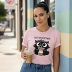 Woman wearing a pink t-shirt with a cat graphic and text, holding a coffee cup on a city street.