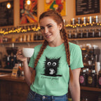 Woman in a coffee shop wearing a green t-shirt with a cat graphic and text, holding a mug.