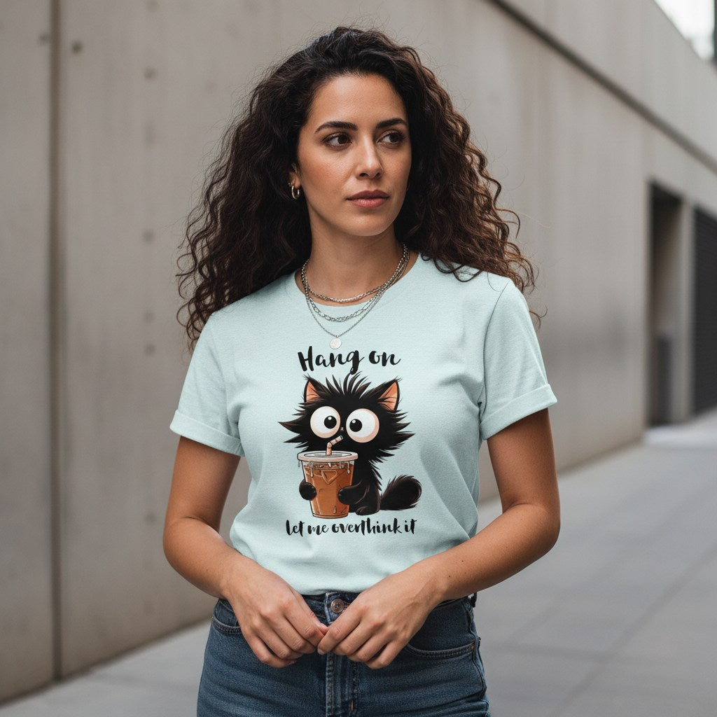 Woman wearing a light blue t-shirt with a cat graphic and text, standing against a concrete wall.