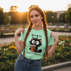 Woman wearing a light green t-shirt with a black cat graphic and text, standing in a park.