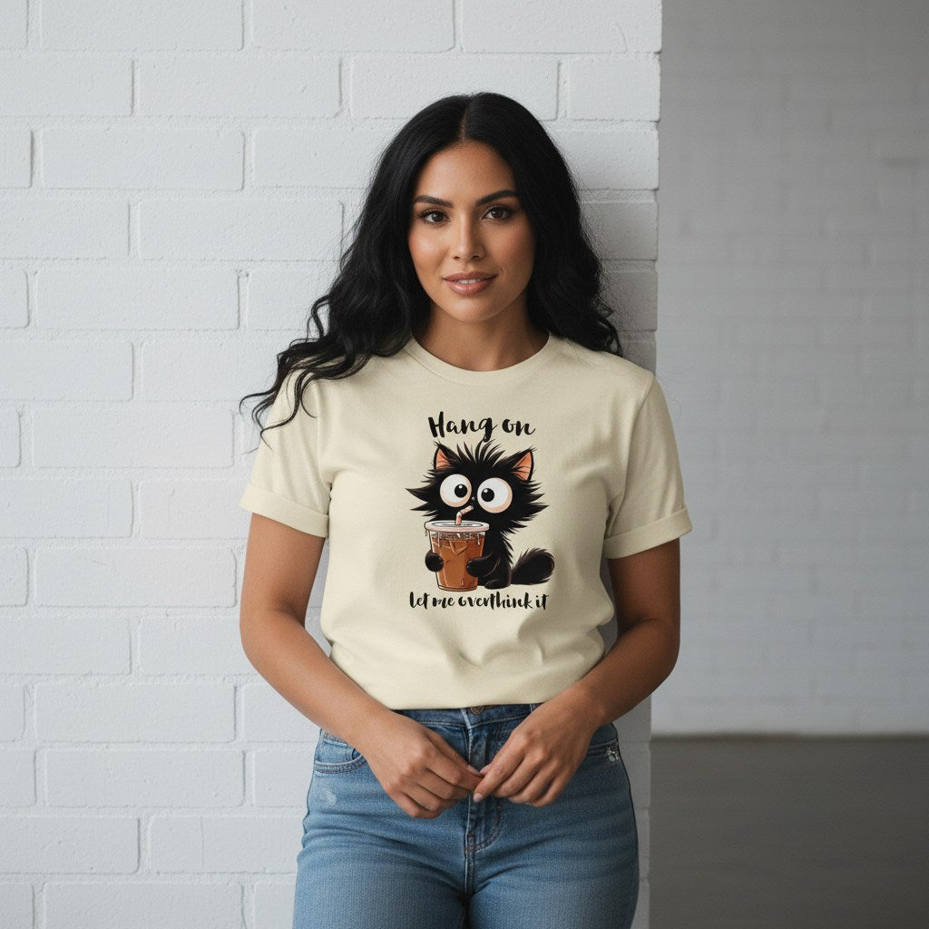 Woman wearing a t-shirt with a cat graphic and text against a white brick wall.