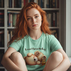 Person wearing a green t-shirt with a teddy bear graphic and text in a room with bookshelves.