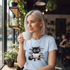 Woman in a cafe holding a cup, wearing a t-shirt with a cat graphic and text.