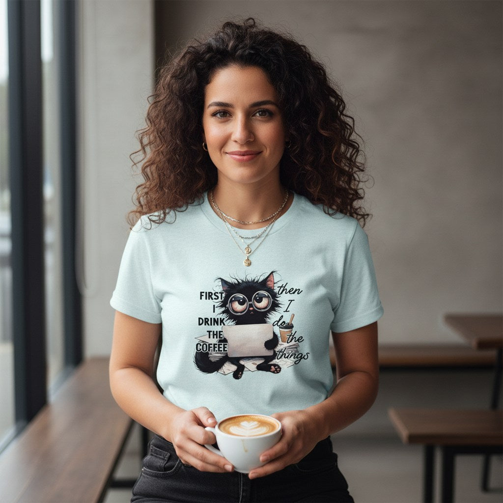 Woman wearing a light blue t-shirt with a cat graphic and text, holding a coffee cup.