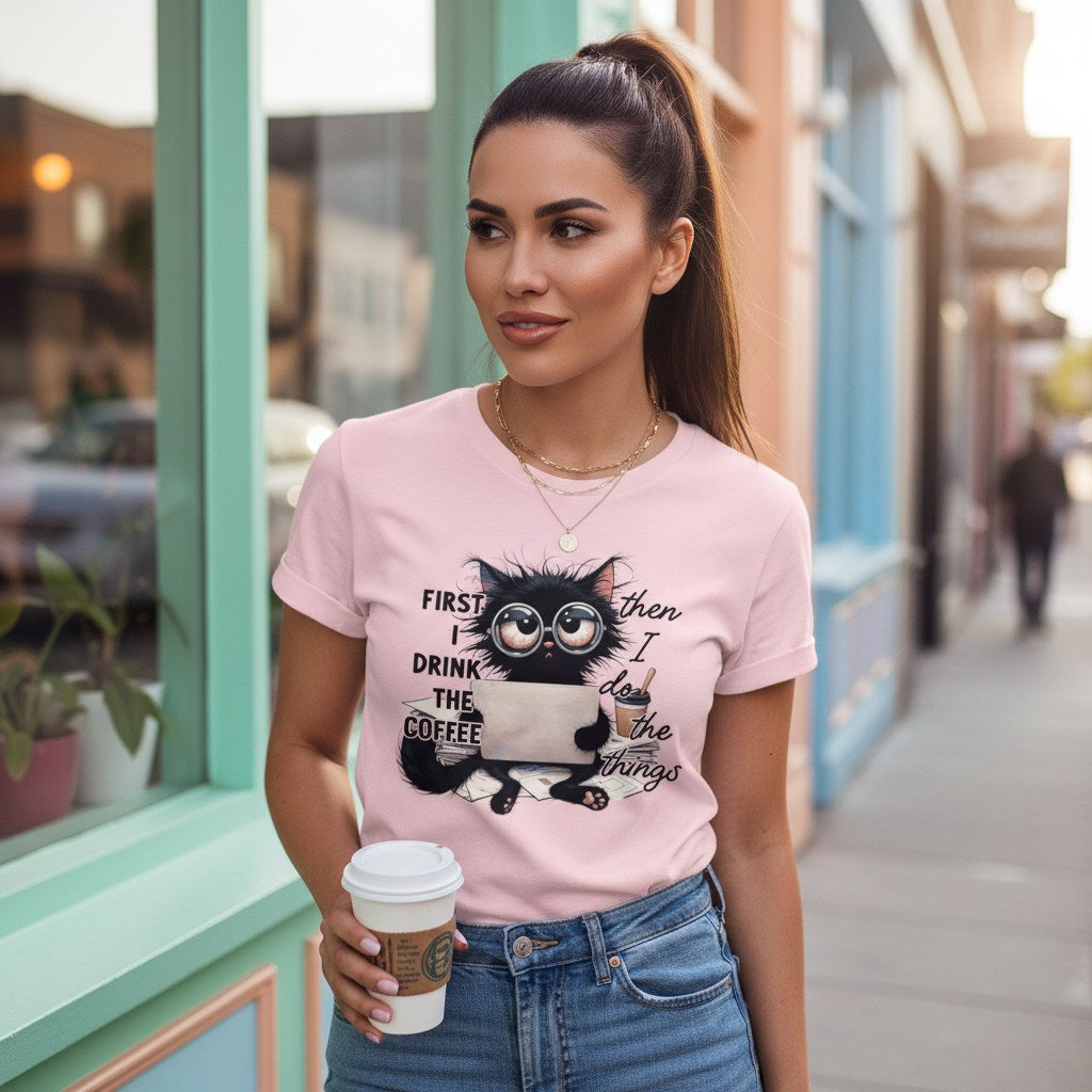 Woman wearing a pink t-shirt with a cat graphic and text, holding a coffee cup on a city street.