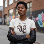Person wearing a t-shirt with a cartoon skunk design and text, standing in an urban setting.