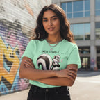 Woman wearing a light green t-shirt with a skunk graphic and text, standing in an urban setting.