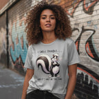 Woman wearing a t-shirt with a skunk graphic and text in front of a graffiti-covered wall.