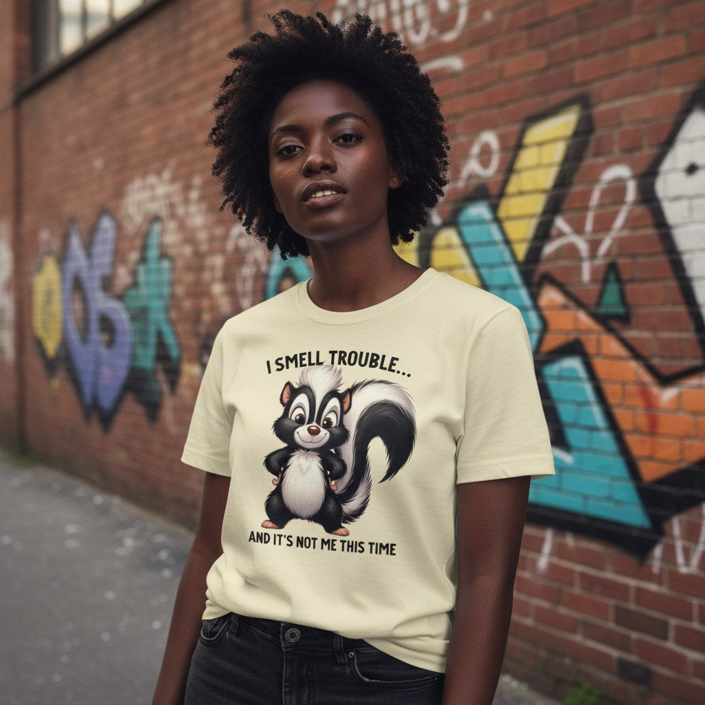 Person wearing a t-shirt with a skunk graphic and text in front of a graffiti-covered wall.