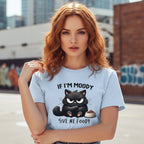 Woman wearing a light blue t-shirt with a black cat graphic and text, standing outdoors.