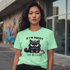 Woman wearing a green t-shirt with a black cat graphic and text in an urban setting.