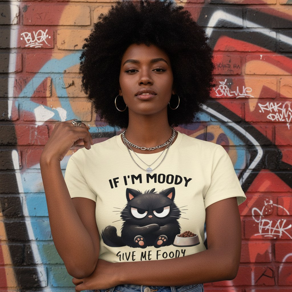 Woman wearing a t-shirt with a cat graphic and text, standing in front of a graffiti-covered wall.