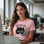 Woman wearing a pink t-shirt with a black cat graphic and text, sitting at a desk in an office.
