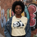 Person wearing a shirt with a panda graphic and text, standing in front of a graffiti-covered wall.