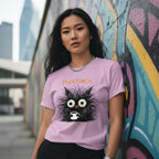 Woman wearing a pink t-shirt with a black cat graphic and text, standing in front of a colorful mural.