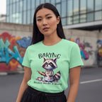 Woman wearing a light green t-shirt with a raccoon graphic and text, standing in an urban setting with graffiti.