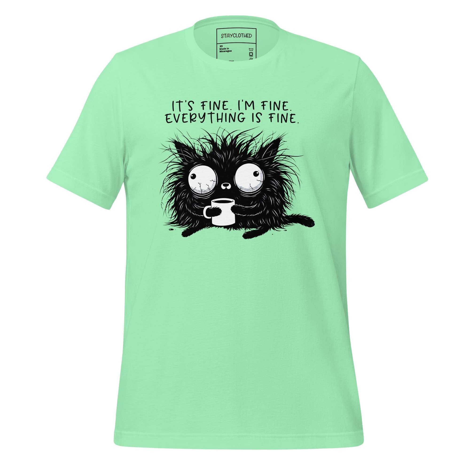 Light green t-shirt with a black cat graphic and text on a wooden surface, featuring the brand 'StayClothed'.