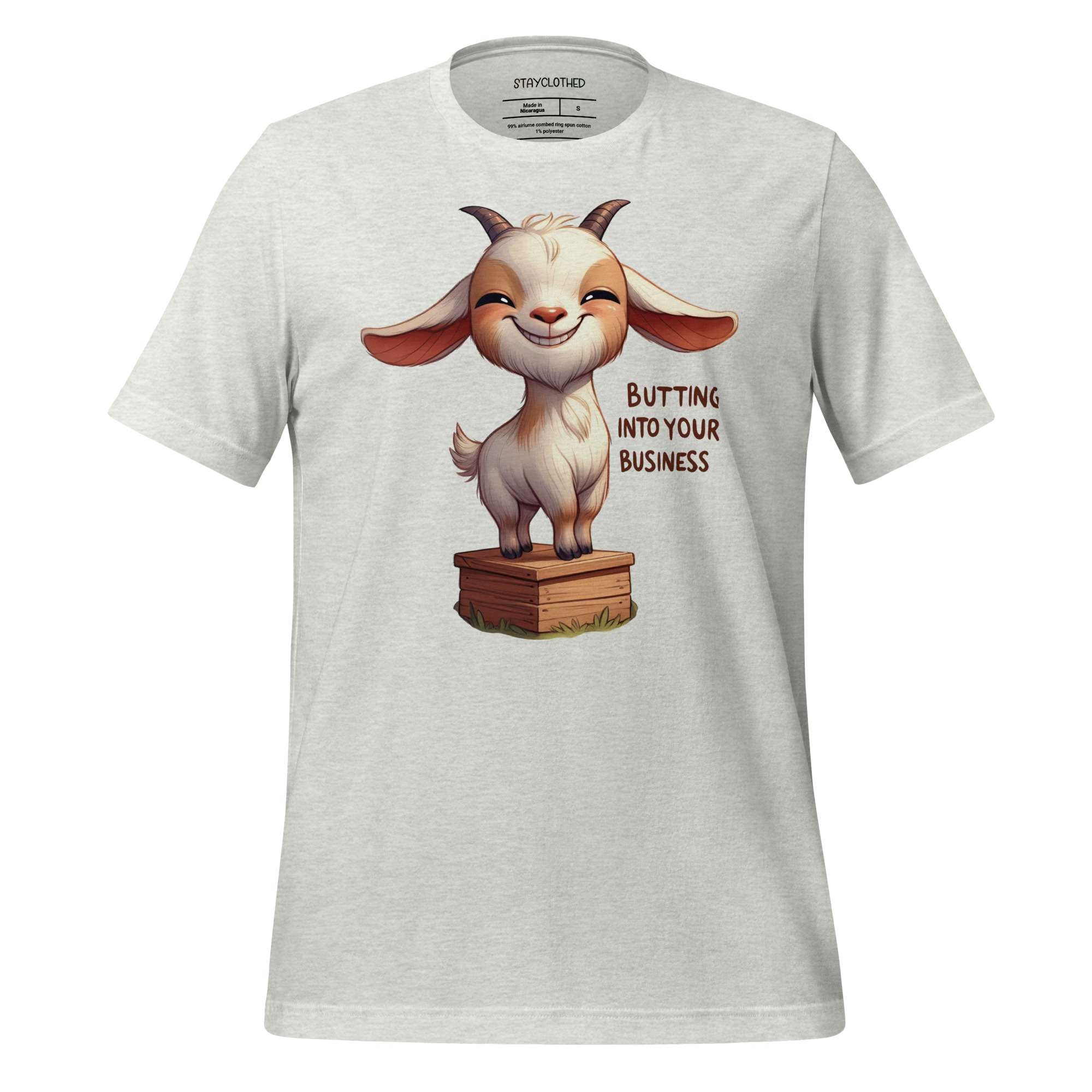 White t-shirt with a cartoon goat graphic and text on a wooden surface, featuring the brand 'StayClothed'.