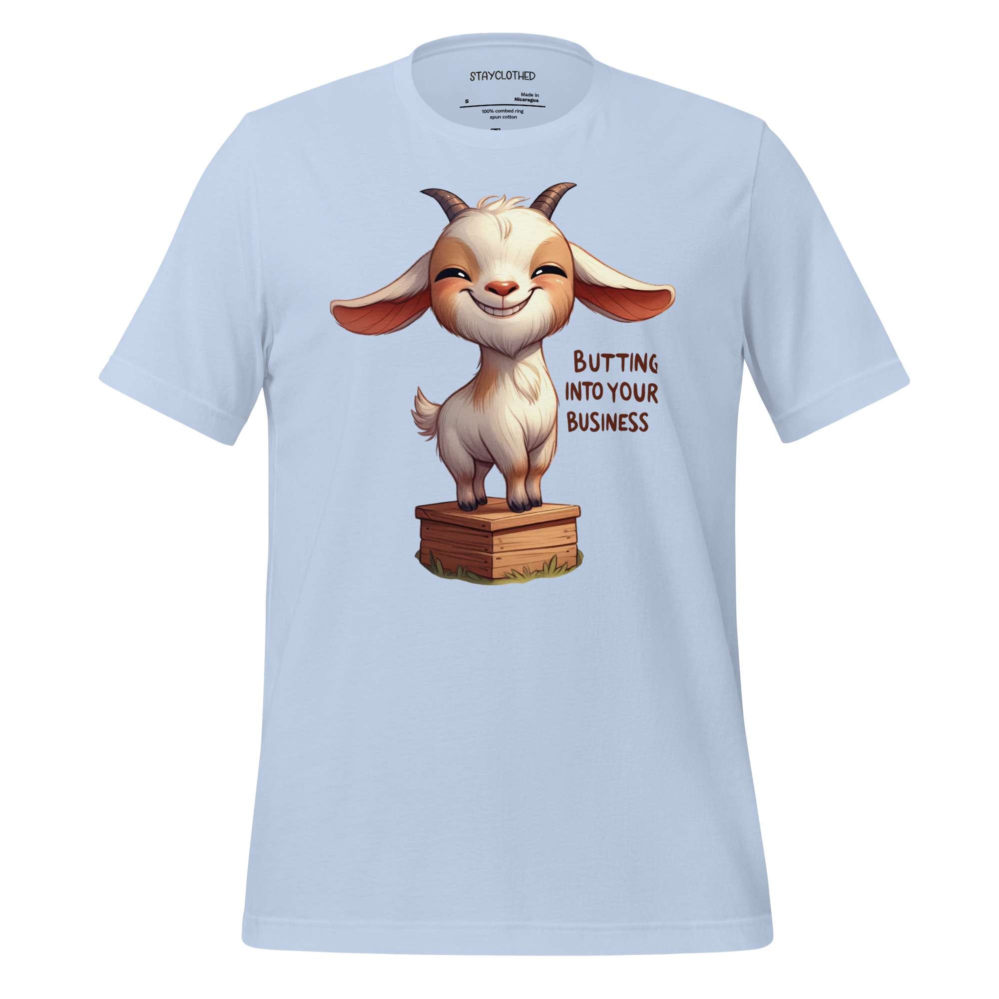 White t-shirt with a cartoon goat graphic and text on a wooden surface, featuring the brand 'StayClothed'.