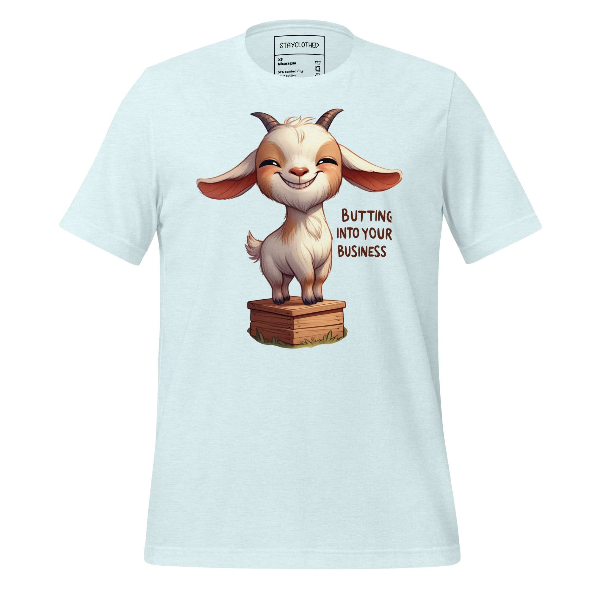 White t-shirt with a cartoon goat graphic and text on a wooden surface, featuring the brand 'StayClothed'.
