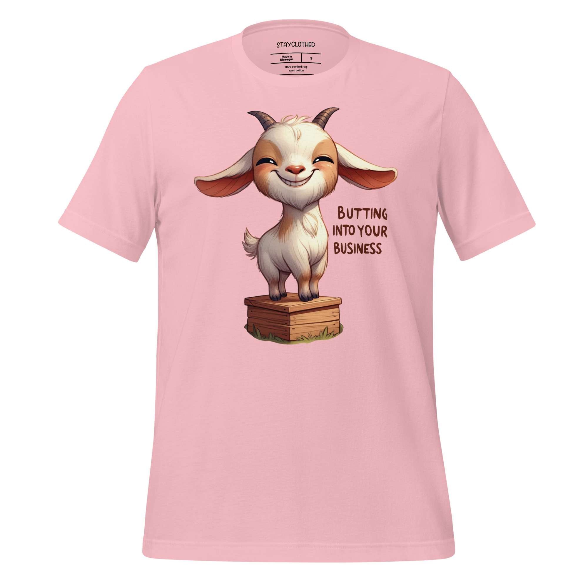 Pink t-shirt with a cartoon goat graphic and text on a wooden surface, featuring the brand 'StayClothed'.