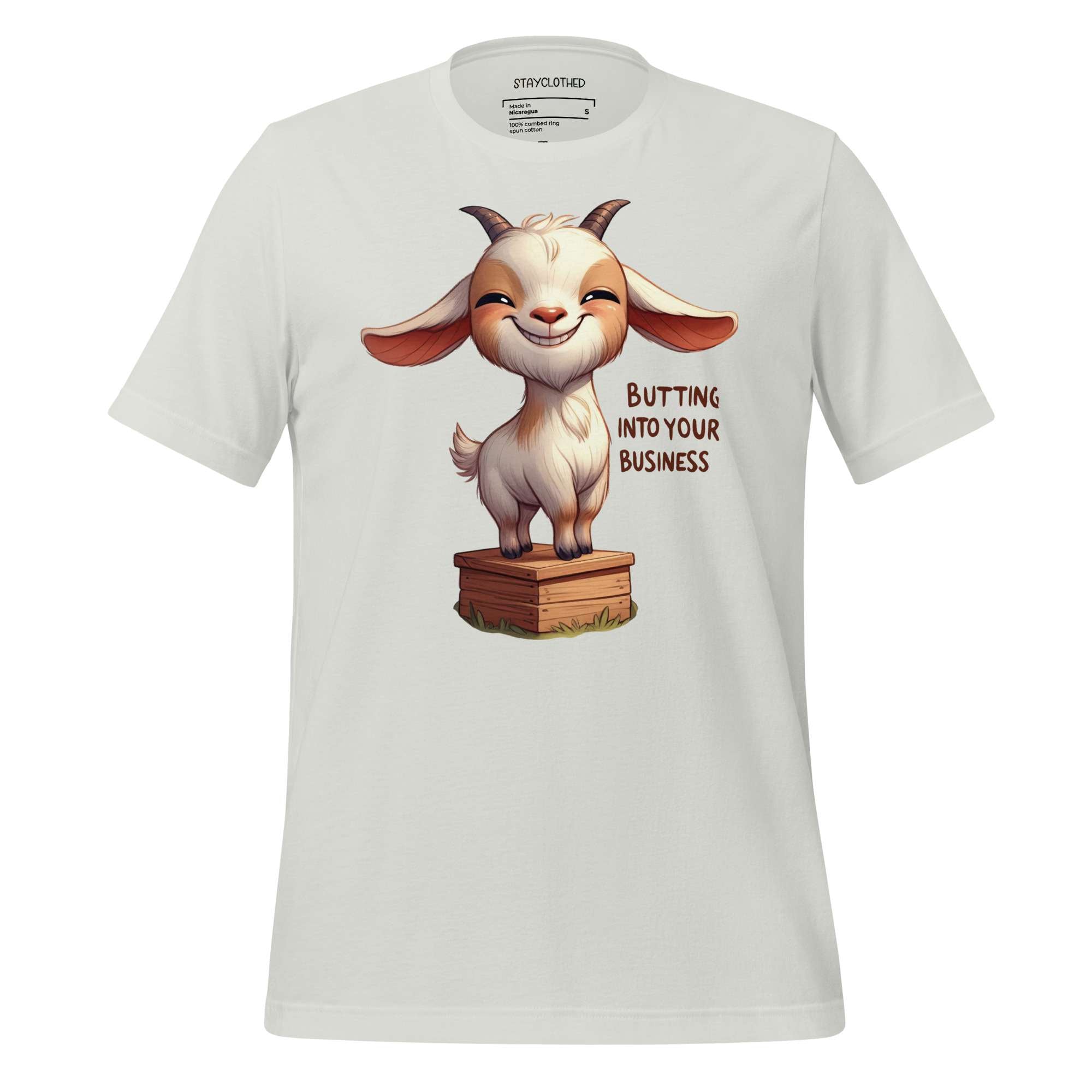 White t-shirt with a cartoon goat graphic and text on a wooden surface, featuring the brand 'StayClothed'.