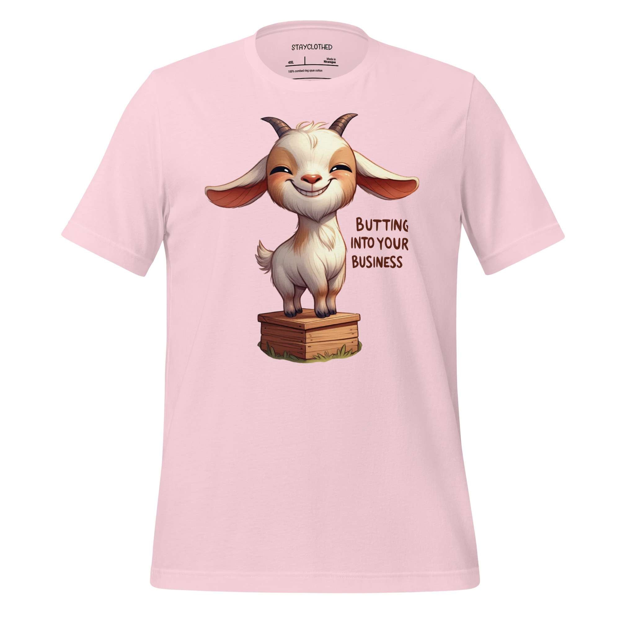 Pink t-shirt with a cartoon goat graphic and text on a wooden surface, featuring the brand 'StayClothed'.