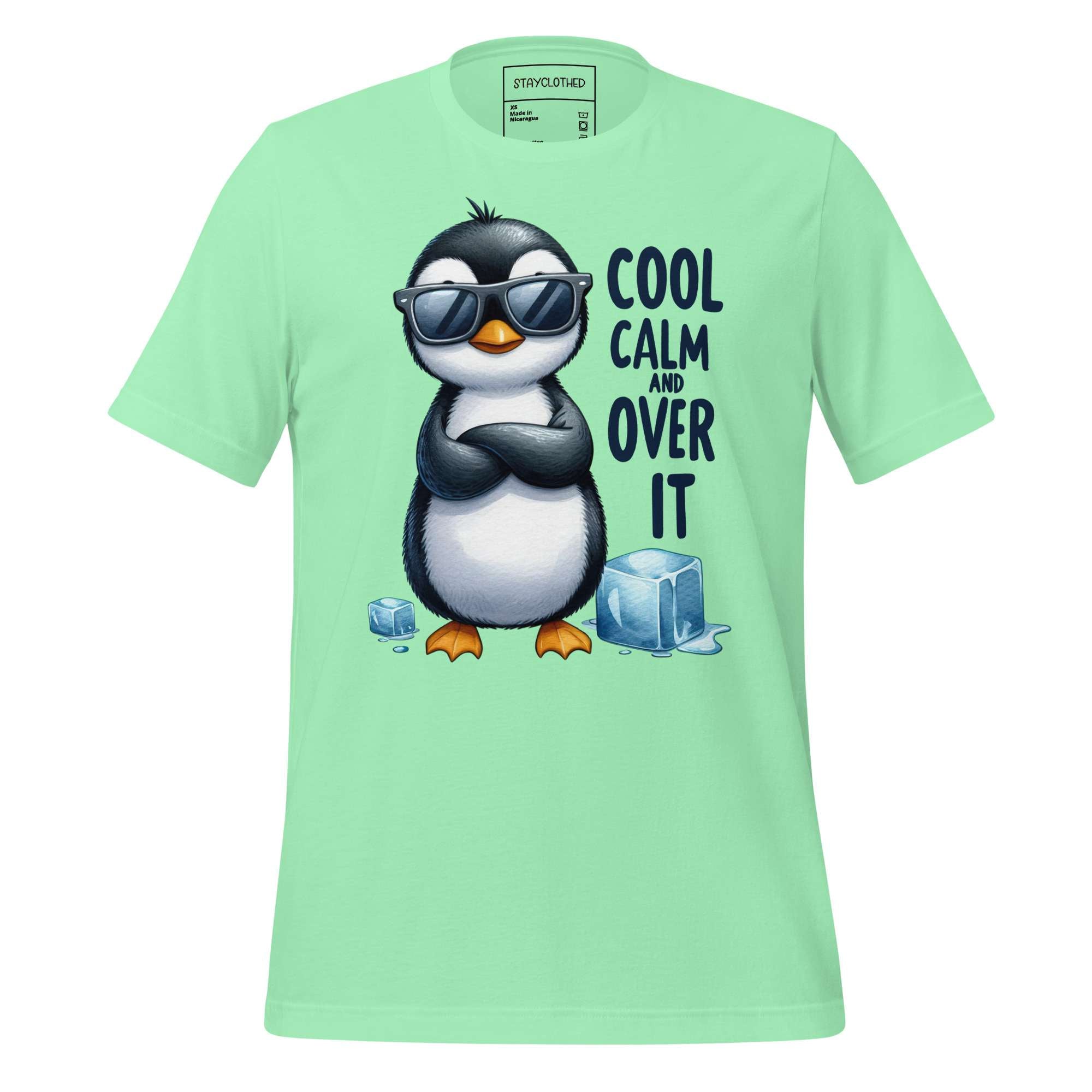Light green t-shirt with a penguin graphic and text on a wooden surface, featuring the brand 'StayClothed'.