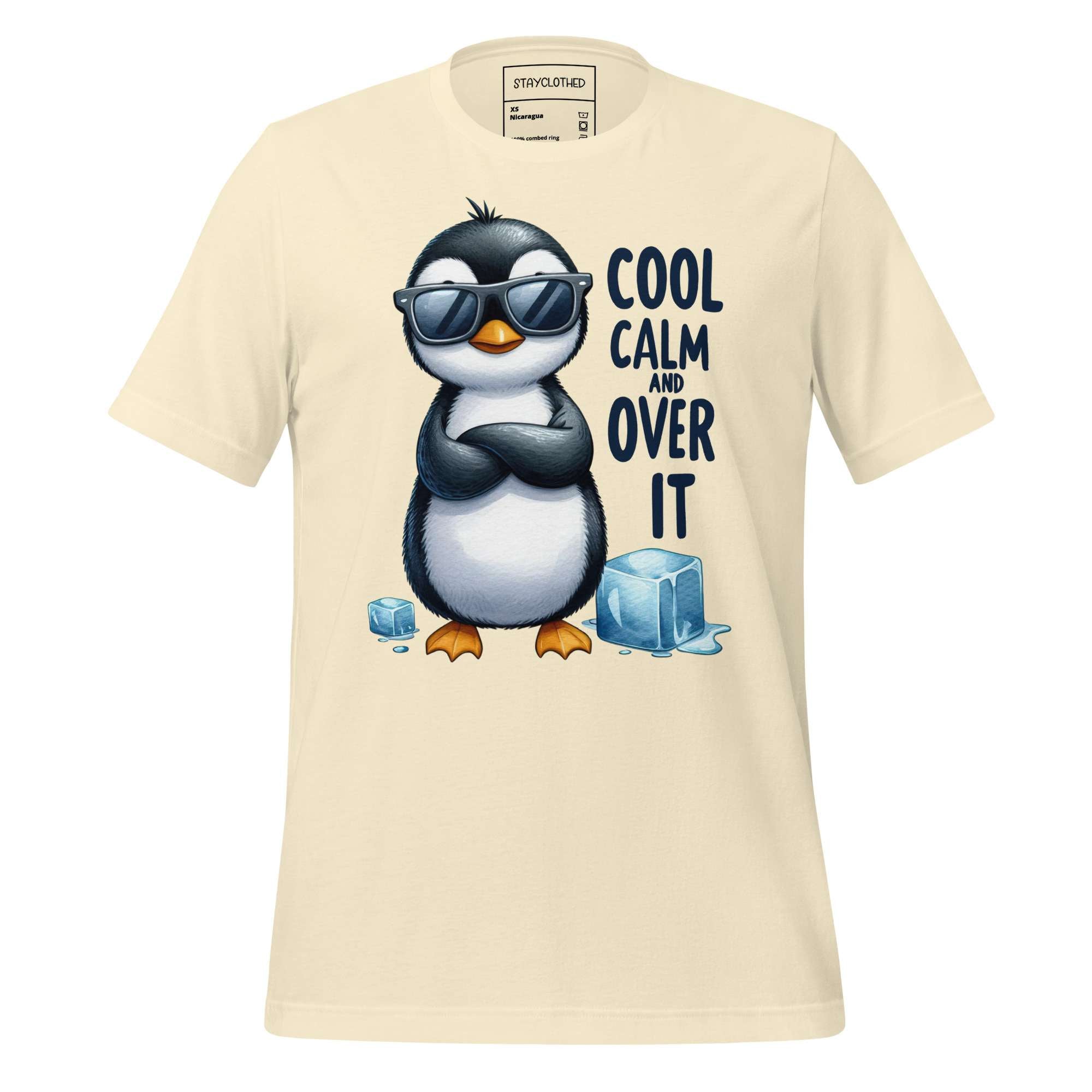 Beige t-shirt with a penguin graphic and text 'Cool Calm and Over It' on a wooden surface, featuring the brand 'StayClothed'.