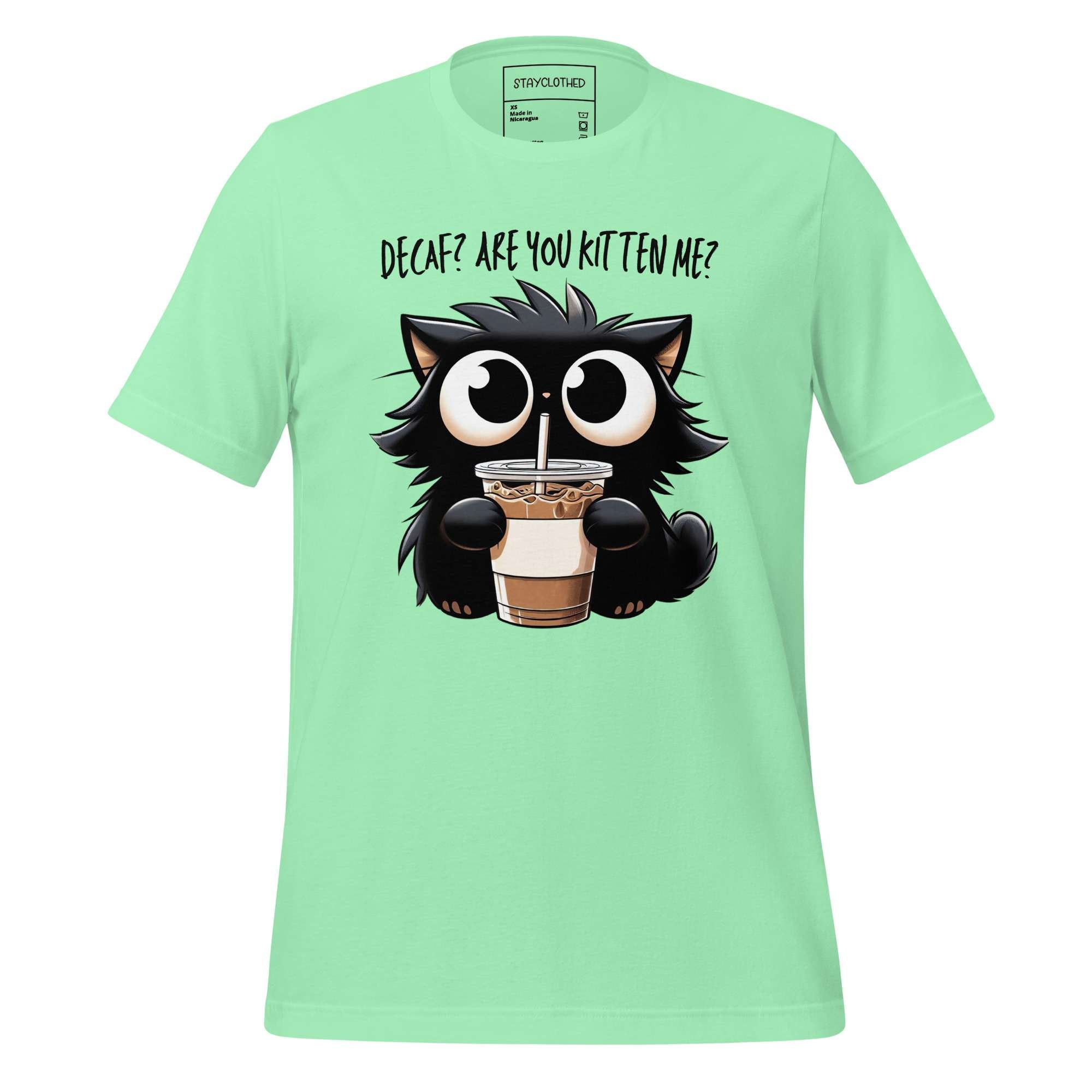 Light green t-shirt with a cartoon cat holding a drink on a wooden surface, featuring the brand 'StayClothed'.