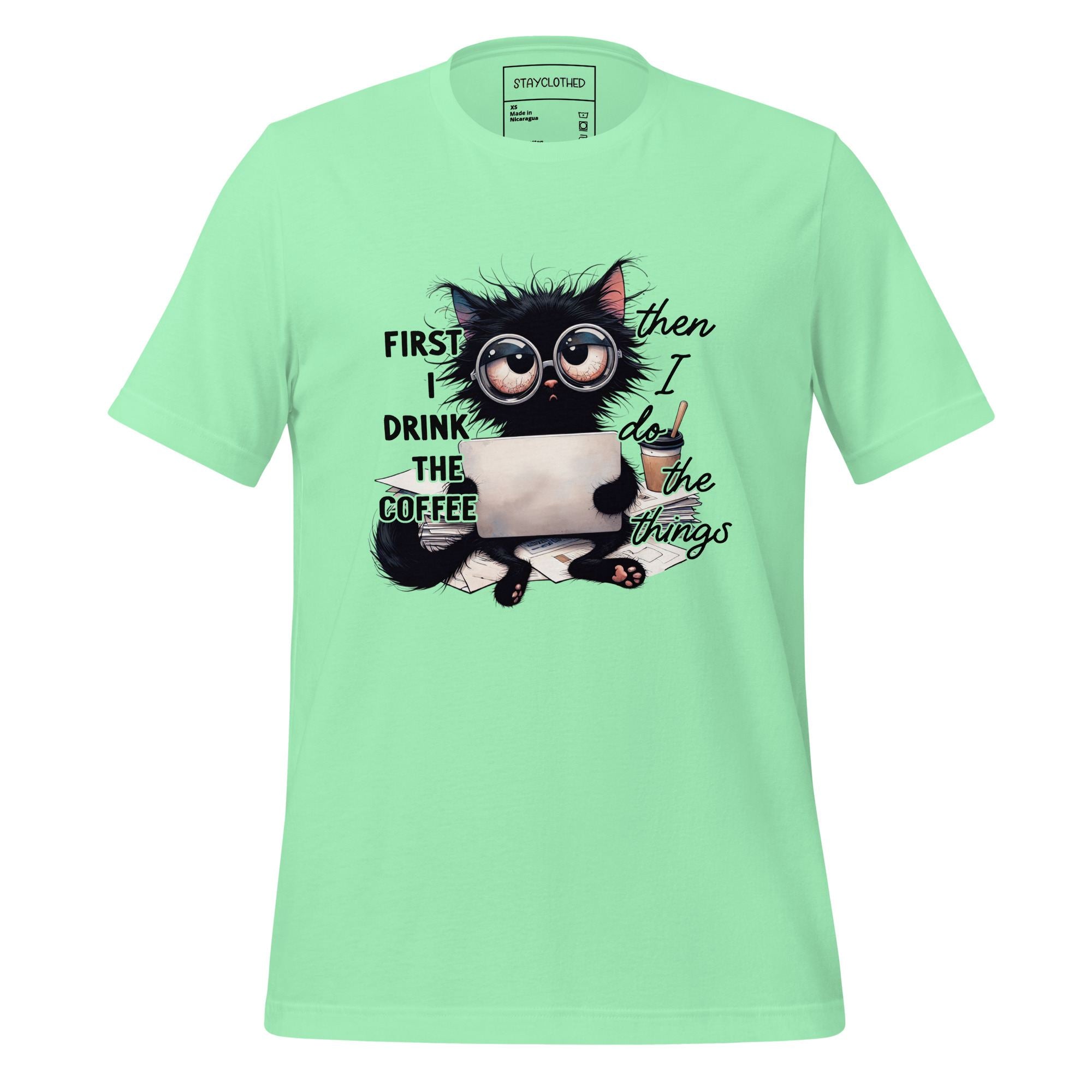 Light green t-shirt with a cat graphic and text on a wooden surface, featuring the brand 'StayClothed'.