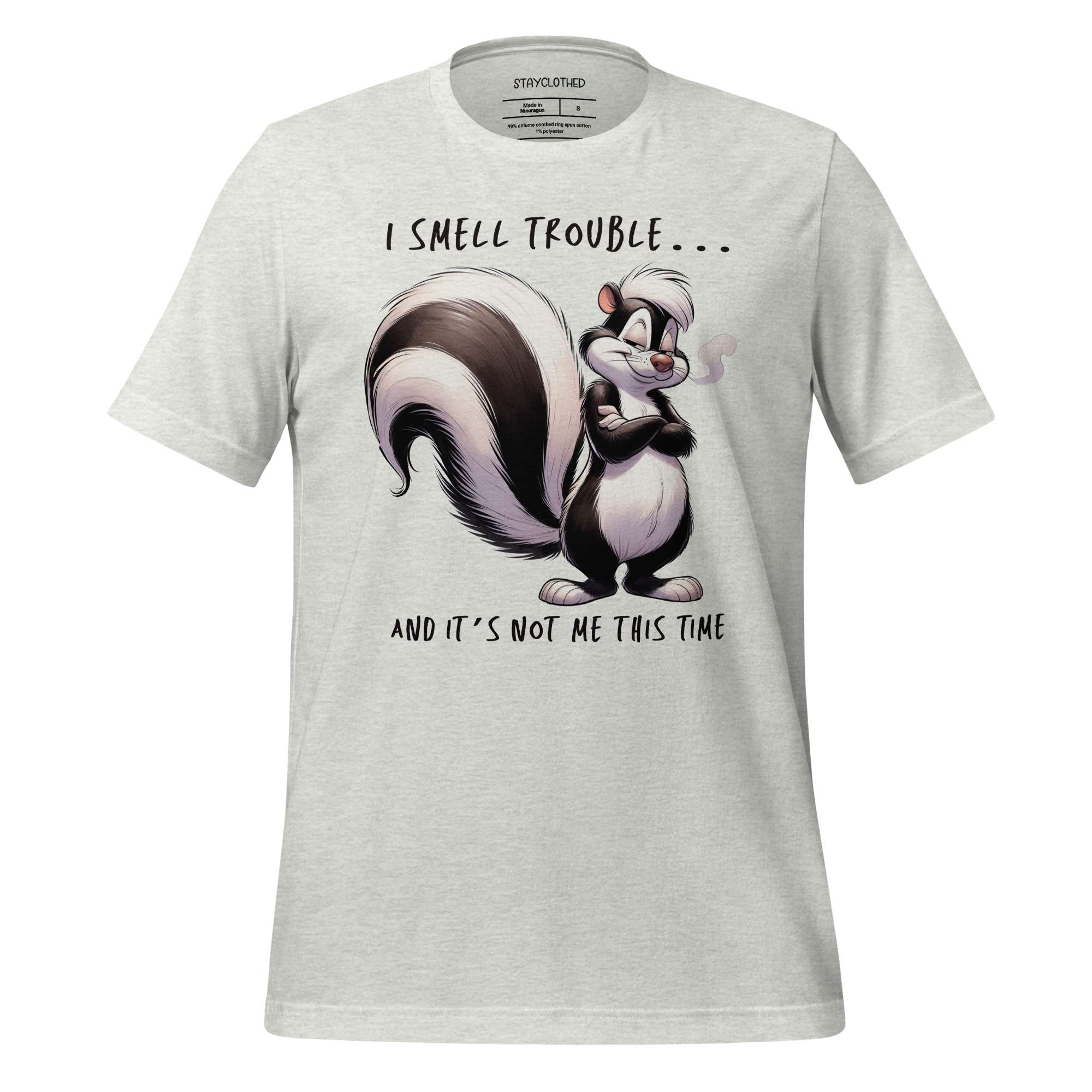 White t-shirt with a cartoon skunk design and text on a wooden surface, featuring the brand 'StayClothed'.