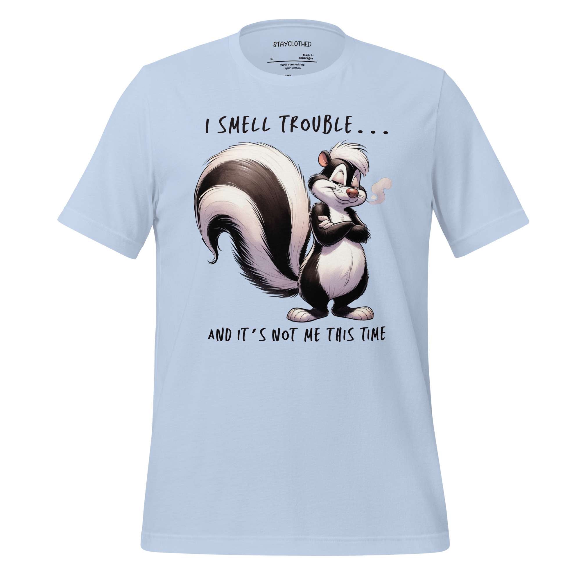White t-shirt with cartoon skunk design and text on a wooden surface, featuring the brand 'StayClothed'.